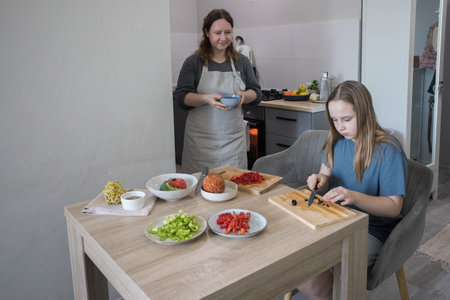 Healthy daughter and her mother cooking in domestic kitchen together, family lifestyle portraitの写真素材