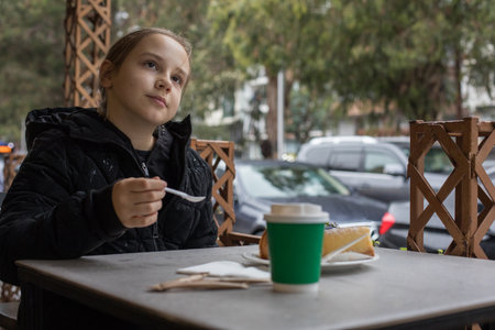 Happy young child girl drinking coffee and eating croissant in city street cafeの写真素材