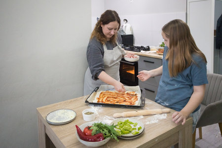 Pretty child girl with woman cooking homemade pizza in domestic kitchen together. Mother and daughterの写真素材