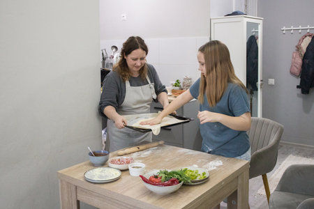Cute daughter cooking pizza with her mother in the kitchenの写真素材