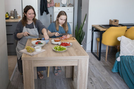 Concentrated daughter and her mother cooking in domestic kitchen together, family lifestyle portraitの写真素材