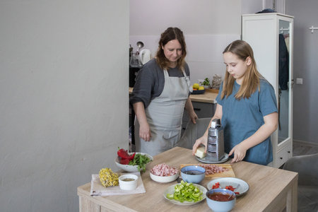 Little daughter and her mother cooking in domestic kitchen together, family lifestyle portraitの写真素材