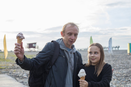 Beautiful child daughter and her father walking and eating ice cream outdoors. Happy family, childhood and weekend conceptの写真素材