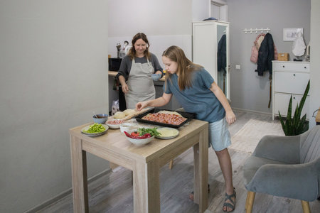 Charming child girl with woman cooking homemade pizza in domestic kitchen together. Mother and daughterの写真素材