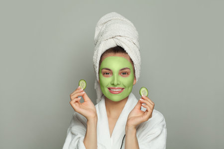 Healthy woman in green organic cosmetic face mask holding cucumber slicesの写真素材