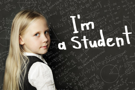 Young school child girl in classroom on chalkboard background. Education and back to school concept