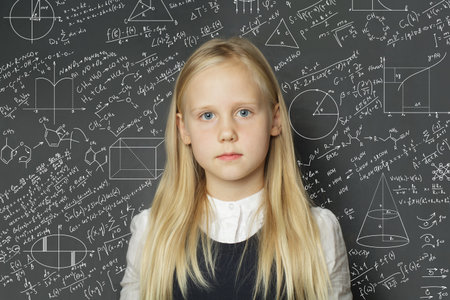 Serious school child girl standing in classroom on blackboard background. Education concept