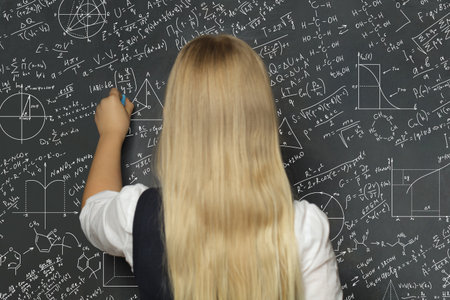 School child girl holding chalk in classroom on blackboard background. Education concept