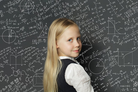 Cheerful school child girl standing in classroom on blackboard background. Education concept