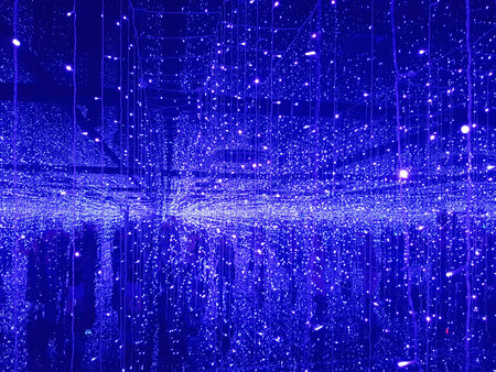 Visitors walk through a space filled with many bright blue lights hanging from above and reflecting on the ground. The lights create a unique atmosphere at the evening gathering.の写真素材