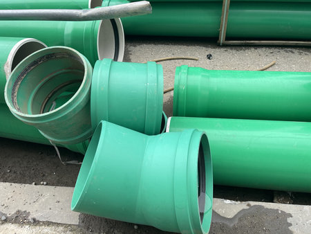 Workers have placed green pipes on the ground at a construction site. Some pipes are upright while...