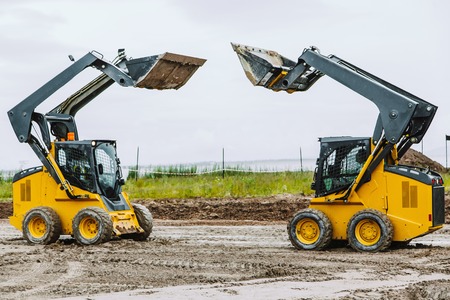 two yellow skid steers with raiced bucket outdoorsの写真素材