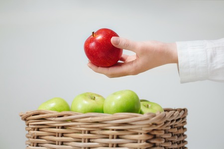 basket with green apples and one red  in handの写真素材