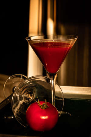 Tomato pouring out of fancy glass next to glass of tomato juiceの写真素材