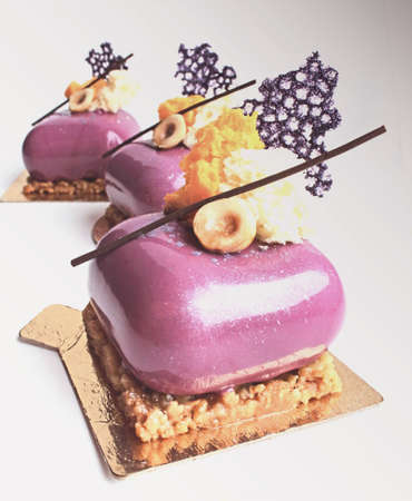 Purple shiny glazed dessert with hazelnut microwave sponge and coral lace crepe decoration on light backgroundの写真素材