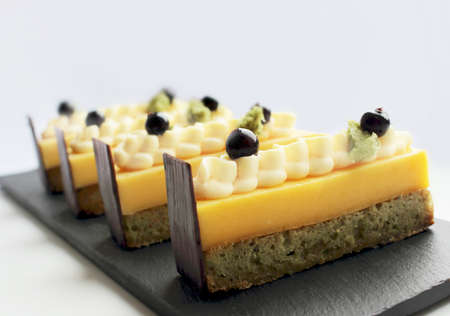 Bright orange and pistachio desserts with black currants and chocolate on light backgroundの写真素材