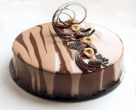 Coffee and chocolate cake with spiral chocolate decoration and hazelnuts on light backgroundの写真素材