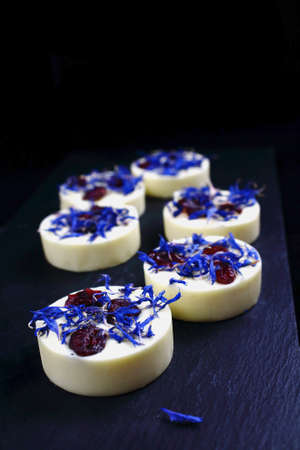 White chocolate pralines with blue knapweed petals and dried cranberries on dark backgroundの写真素材