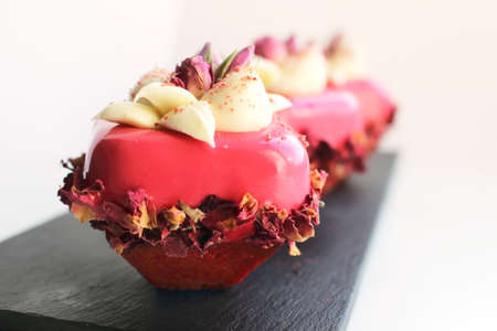 Pink rose bouquet desserts with cream and dried edible flowers on dark plate and white backgroundの写真素材