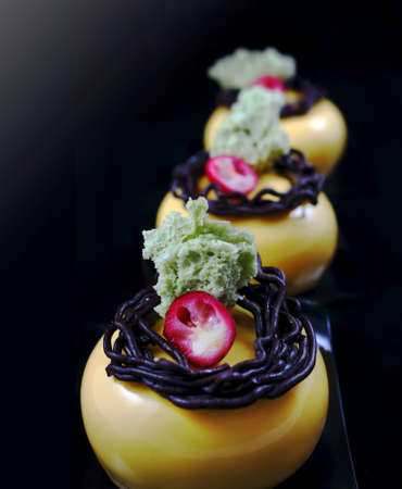 Yellow round desserts with chocolate nest decoration, cranberries and pistachio spongeの写真素材