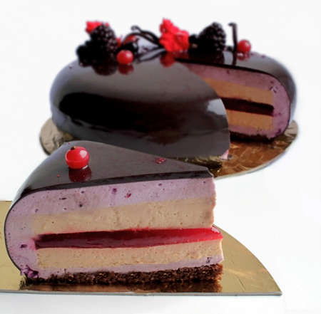 Slice of layered mousse chocolate cake with shiny mirror glaze, red currants, black currants and blackberriesの写真素材