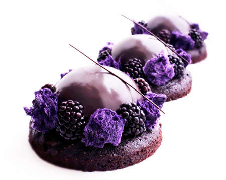 Purple chocolate desserts with shiny mirror glaze and blackberries on white backgroundの写真素材