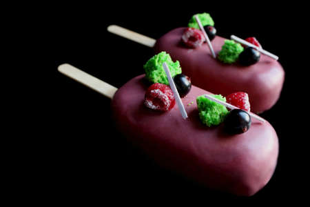 Pink glazed berry gelato ice cream on stick with raspberry, pistachio sponge and black currantsの写真素材