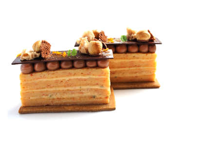 Two orange Opera cake slices with hazelnuts, cookie and ganache isolated on white backgroundの写真素材