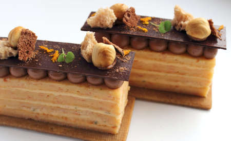 Two orange Opera cake slices with hazelnuts and ganache on cookie base isolated on white backgroundの写真素材