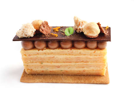 Orange Opera cake slice with hazelnuts, cookie and ganache isolated on white backgroundの写真素材