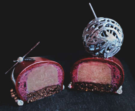 Sliced dark chocolate berry dessert with silver wool ball decoration and brownie on black backgroundの写真素材