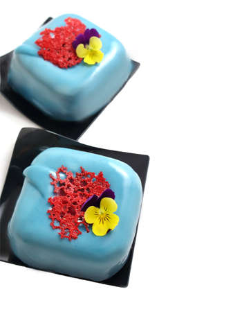 Light blue square desserts with red coral lace crape and edible flower isolated on white backgroundの写真素材