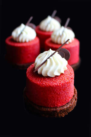 Four red textured desserts with cream top and chocolate decorations isolated on black backgroundの写真素材
