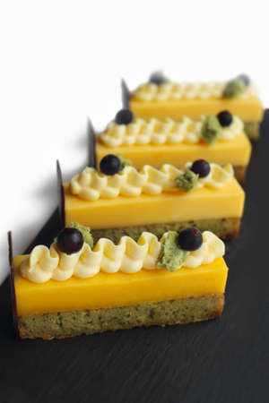 Orange mousse and pistachio sponge cake slices with piped buttercream and black currantsの写真素材