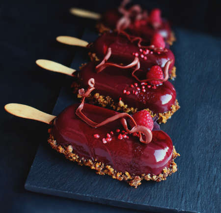 Red fruit ice cream on stick with raspberry and flower petalsの写真素材