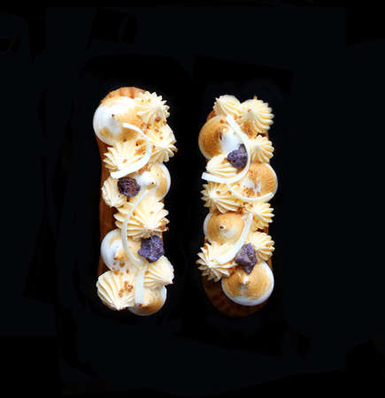 Lemon pie eclairs with purple crumble, citrus ganache and meringue top view on black backgroundの写真素材