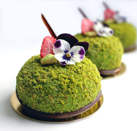 Close up of green textured pistachio desserts with edible pansy flowers and dried strawberriesの写真素材
