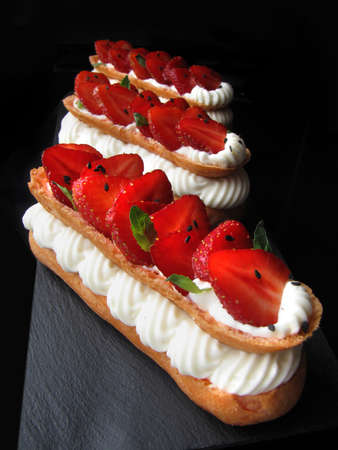 Strawberries and cream eclairs with fresh berries and mint leaves on black backgroundの写真素材