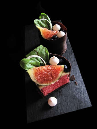 Sliced fig desserts with beetroot leaves, blueberries, meringues and chocolate borderの写真素材