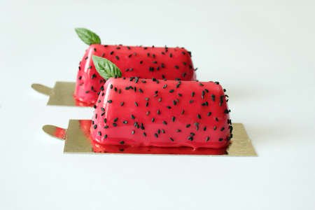 Red watermelon glazed desserts with black sesame seeds and basil leaves on golden coastersの写真素材