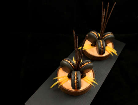 Orange chocolate tarts with black french macarons, chocolate decorations and persimmon on black backgroundの写真素材