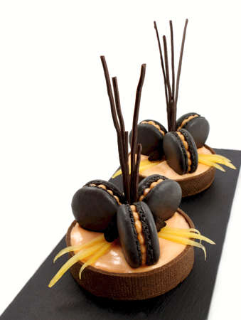 Orange chocolate tarts with black french macarons and persimmon on white backgroundの写真素材