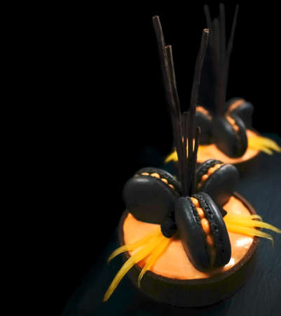 Orange chocolate tarts with black french macarons and persimmon isolated on black backgroundの写真素材