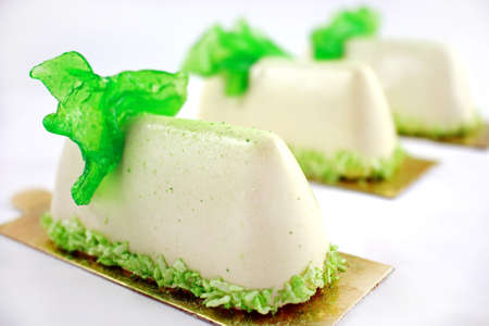 Three white desserts with green caramel decoration and coconutの写真素材
