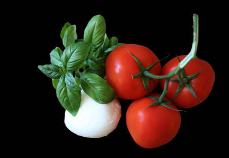 Tomatoes mozzarella cheese and basil salad ingredients isolated on black backgroundの写真素材