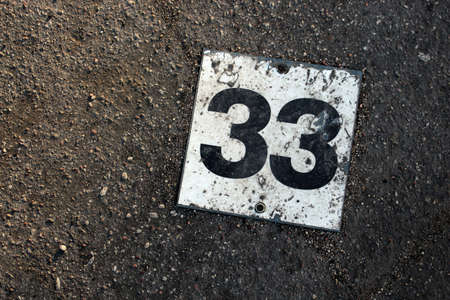 Old rusty parking lot number plate with black and white number on concrete backgroundの写真素材