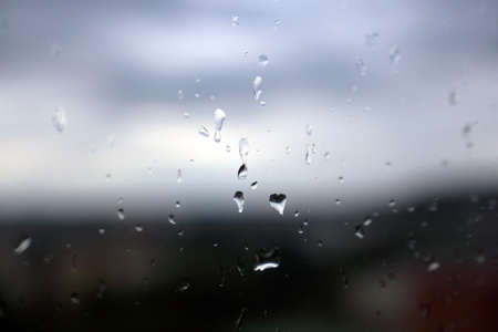 Few big rain drops on window glass on blue sky and city background