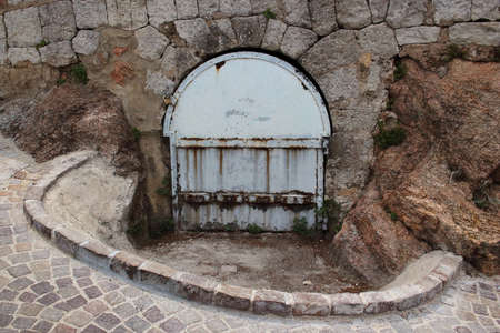 Stone road going down to a cellar with old rusty metal arched door