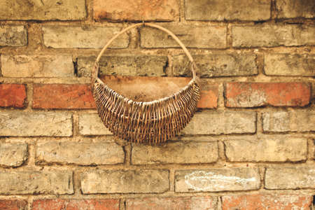 Old yellow brick wall background with hanging round woven basketの写真素材