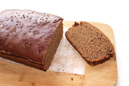 Sliced dark rye hemp seed bread on paper and wooden board on white background